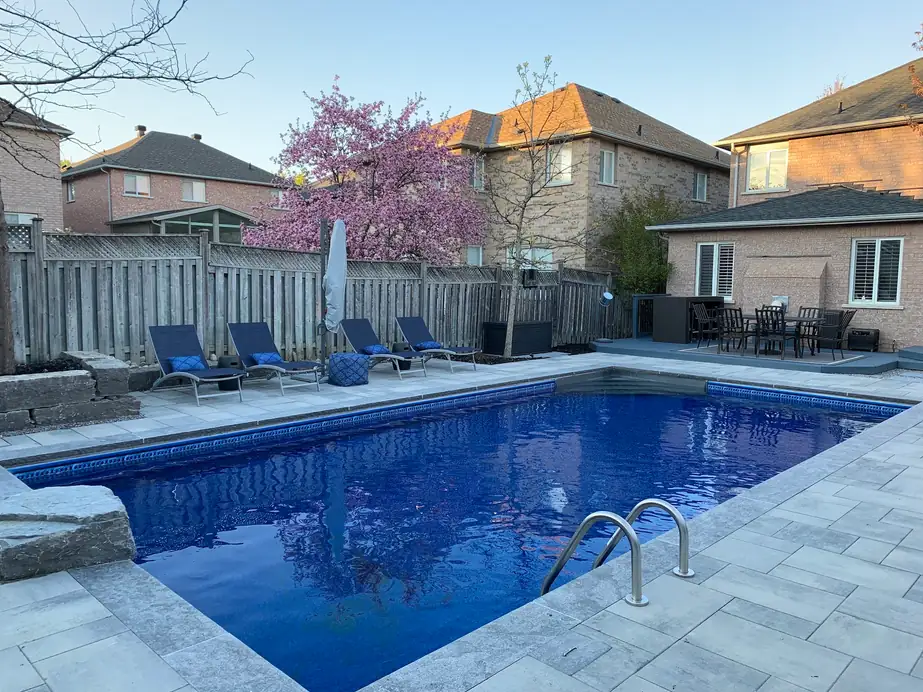 Rectangular inground pool with a deep blue liner, light stone coping and a stainless rail ladder
