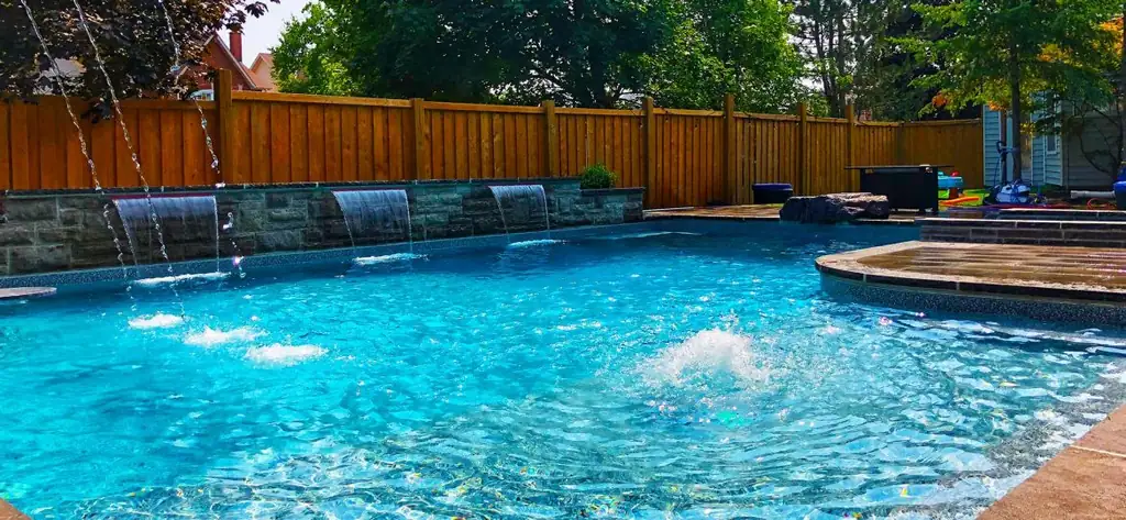 Pool with sheer descent water features and fountain jets in front of a cedar fence
