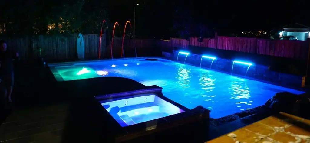 Lit pool at night with a spa, blue LED lights and laminar jets