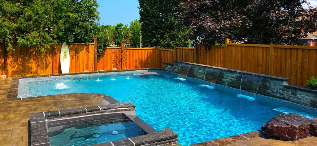 Pool with a stone sheer-descent wall and a raised spa beside a cedar fence