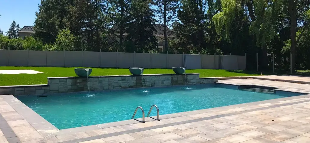 Wide pool with bowl fountains along a stone wall and a lawn